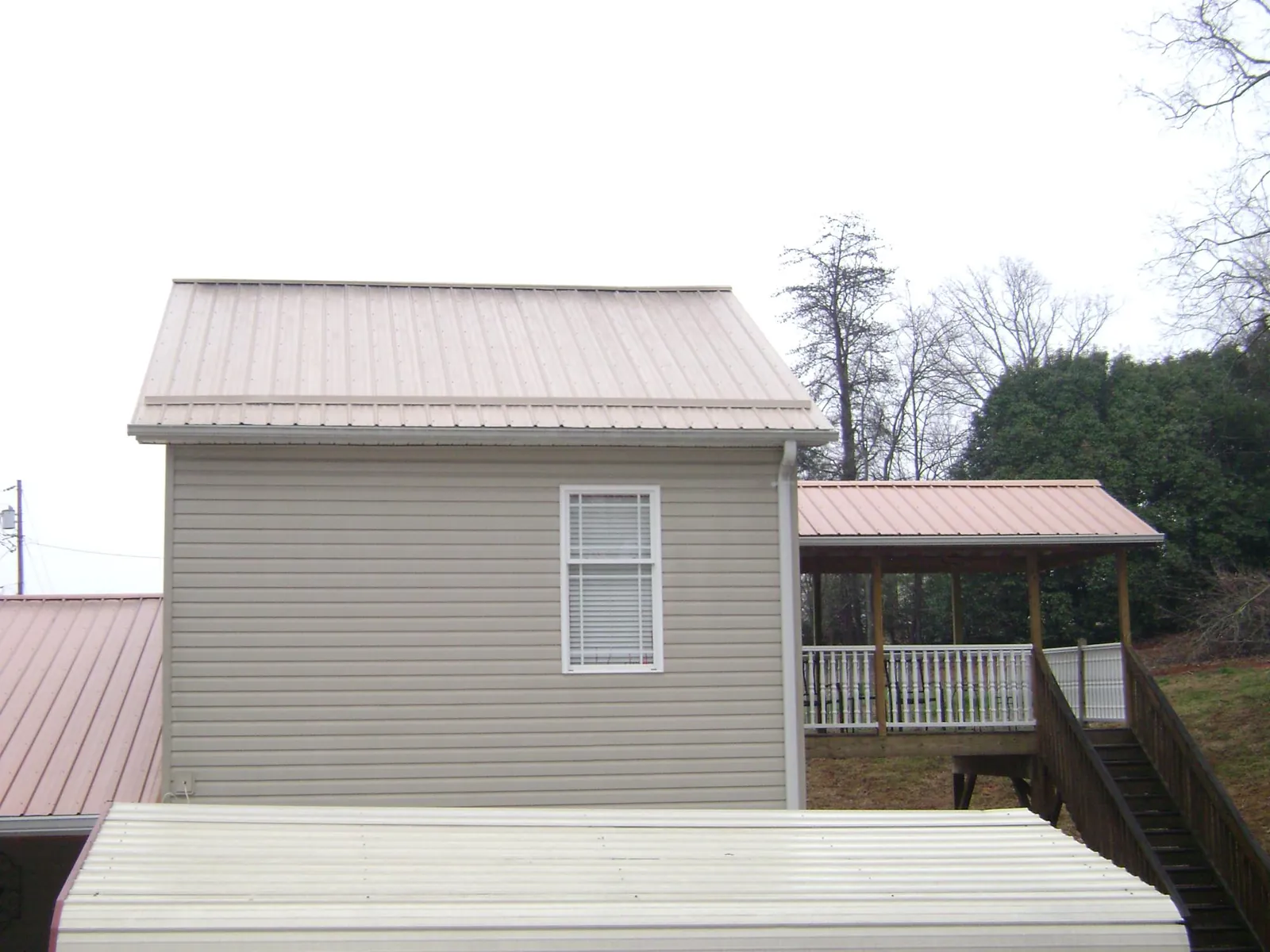 Tan metal roofs on a two story addition and attached porch, from a Roof Replacement job in Melrose